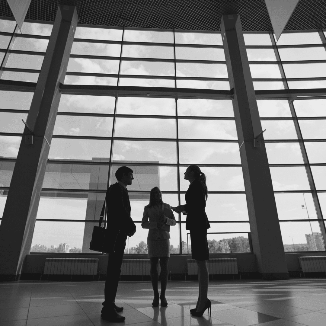 Three people standing in front of a large window.