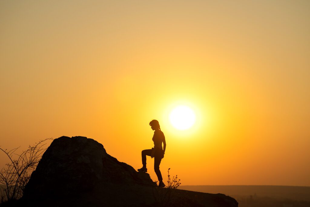 A person standing on top of a rock at sunset.