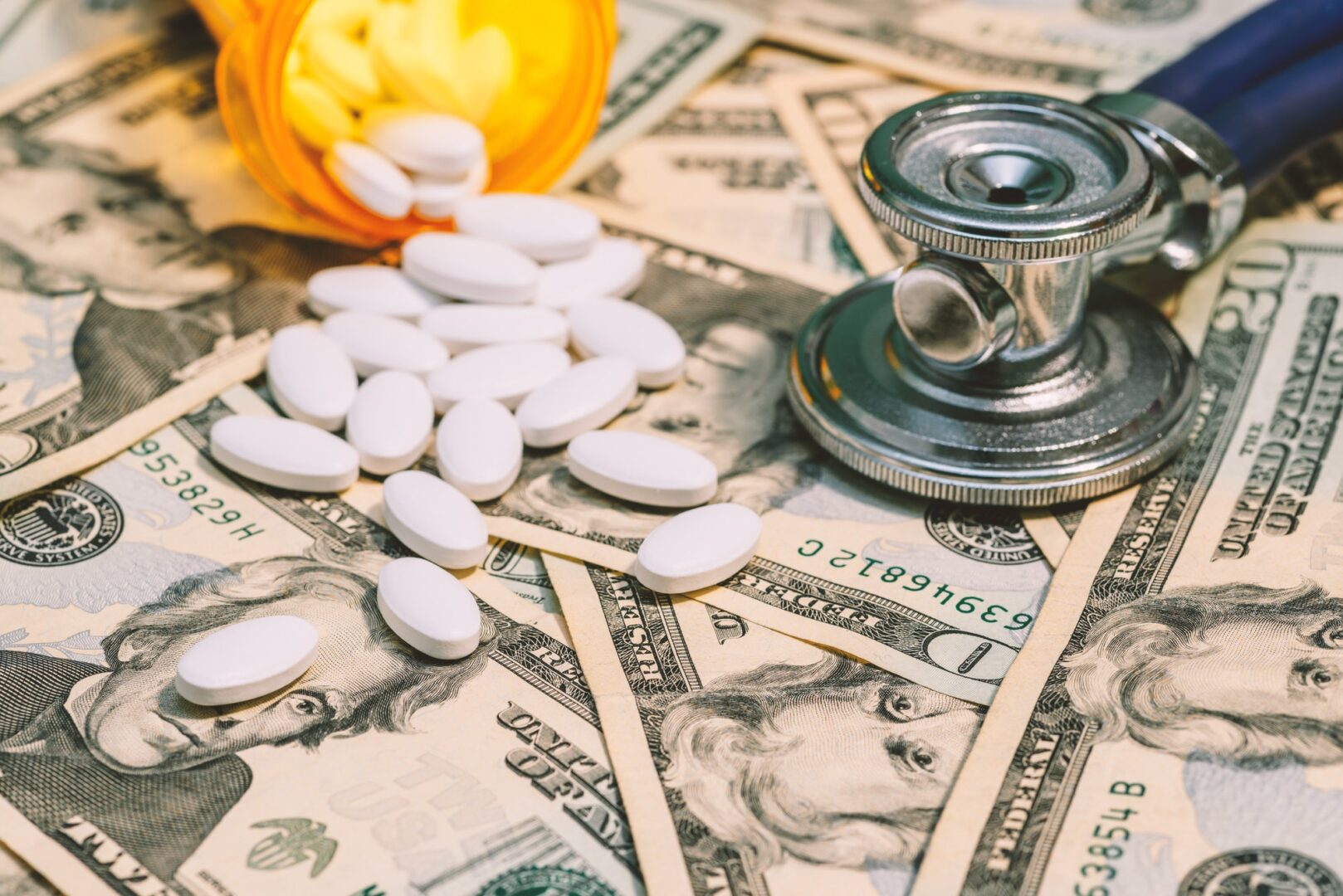 A pile of money sitting next to pills and a stethoscope.